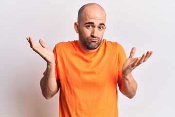 Naklejka premium Young handsome bald man wearing casual t shirt clueless and confused with open arms, no idea and doubtful face.