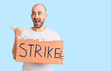 Young handsome man holding strike banner pointing thumb up to the side smiling happy with open mouth