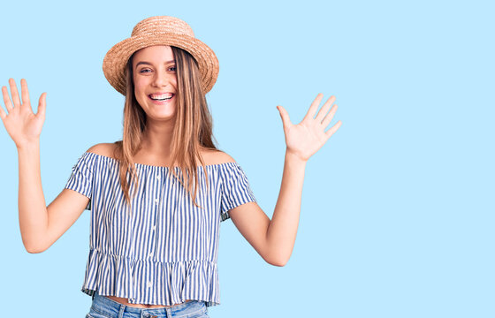 Young beautiful girl wearing hat and t shirt showing and pointing up with fingers number ten while smiling confident and happy.
