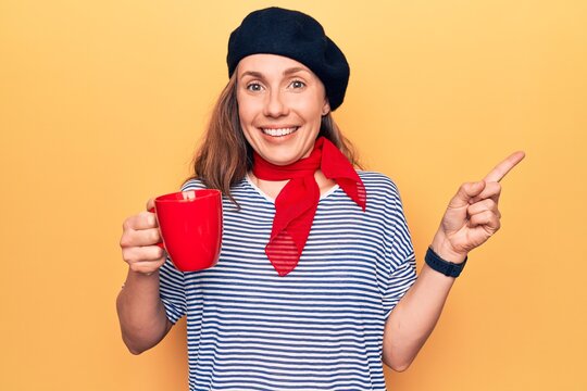 Young beautiful blonde woman wearing fashion beret drinking a cup of coffee smiling happy pointing with hand and finger to the side