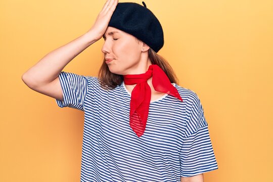 Young beautiful blonde woman wearing french fashion style with scarf and beret surprised with hand on head for mistake, remember error. forgot, bad memory concept.