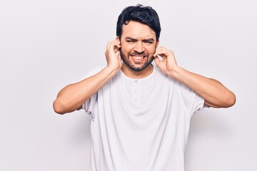 Fototapeta premium Young hispanic man wearing casual clothes covering ears with fingers with annoyed expression for the noise of loud music. deaf concept.