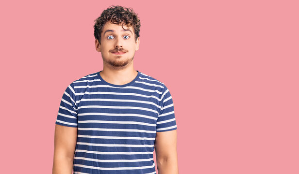 Young handsome man with curly hair wearing casual clothes puffing cheeks with funny face. mouth inflated with air, crazy expression.