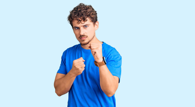 Young handsome man with curly hair wearing casual clothes ready to fight with fist defense gesture, angry and upset face, afraid of problem