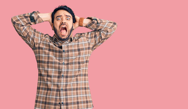 Young hispanic man wearing casual clothes crazy and scared with hands on head, afraid and surprised of shock with open mouth