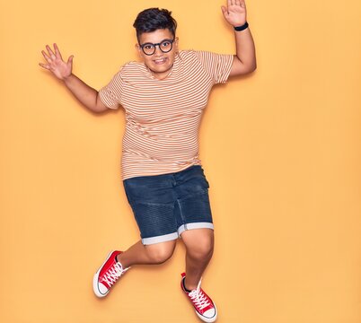 Adorable kid wearing casual clothes and glasses smiling happy. Jumping with smile on face over isolated yellow background