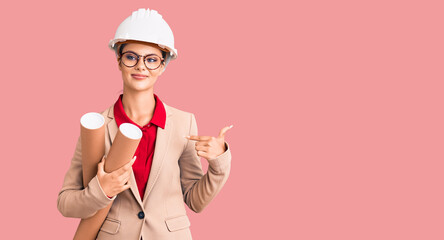 Young beautiful woman wearing architect hardhat and glasses holding blueprints pointing finger to one self smiling happy and proud