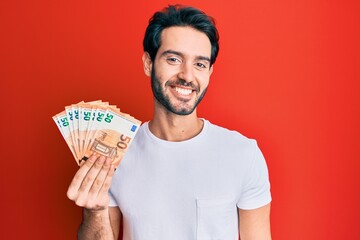 Young hispanic man holding euro banknotes looking positive and happy standing and smiling with a...