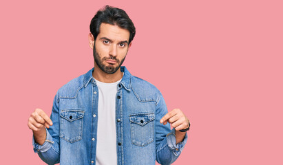 Fototapeta premium Young hispanic man wearing casual clothes pointing down looking sad and upset, indicating direction with fingers, unhappy and depressed.