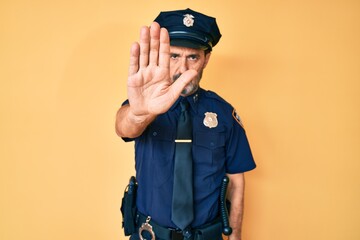 Middle age hispanic man wearing police uniform doing stop sing with palm of the hand. warning expression with negative and serious gesture on the face.