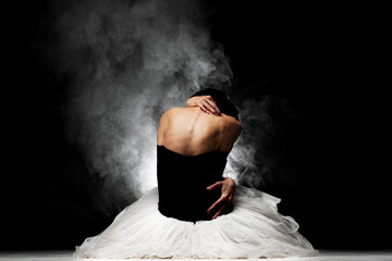 ballerina with a tutu sitting on the floor, posing with smoke in the background