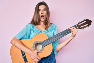 Fototapeta premium Beautiful caucasian woman playing classical guitar afraid and shocked with surprise and amazed expression, fear and excited face.