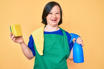 Brunette woman with down syndrome wearing apron holding scourer winking looking at the camera with sexy expression, cheerful and happy face.