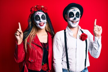 Couple wearing day of the dead costume over red pointing finger up with successful idea. exited and happy. number one.