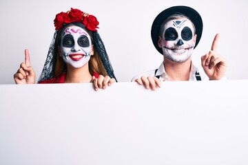 Fototapeta na wymiar Couple wearing day of the dead costume holding blank empty banner surprised with an idea or question pointing finger with happy face, number one