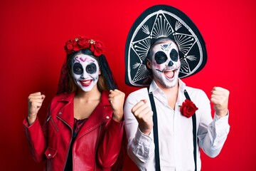 Couple wearing day of the dead costume over red screaming proud, celebrating victory and success very excited with raised arms