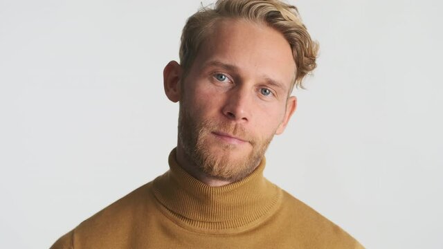 Handsome blond bearded man confidently looking in camera over white background. Male model posing in studio
