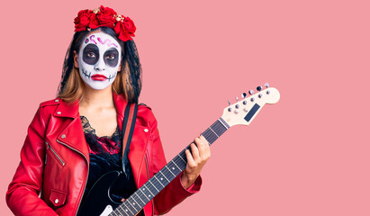 Obraz na płótnie Canvas Woman wearing day of the dead costume playing electric guitar thinking attitude and sober expression looking self confident