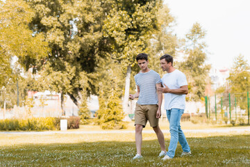 man gesturing while walking and talking with teenager son in park