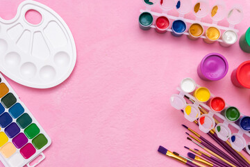 Watercolor paints, gouache, brushes and palette for drawing on a pink background. Copy space.