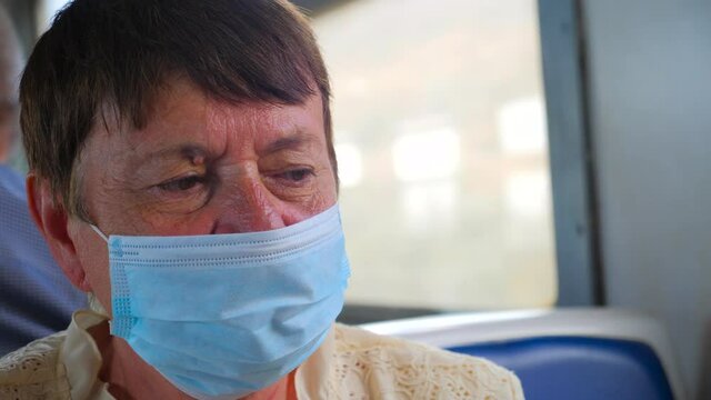 Exhausted tired old woman wearing facemask, protective mask. Wearing disposable blue medical mask in public transport. Respiratory disease protection. Social distancing on coronavirus outbreak