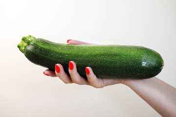 woman holding zucchini in manicured hand