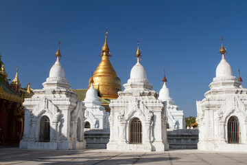 Fototapeta na wymiar Oranate small white pagodas surrounding a large gold plated pagoda.