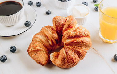 Breakfast table with croissants, coffee, orange juice and blueberries