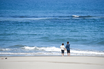 8月末、夏を惜しみ海を見つめるカップルの後ろ姿
