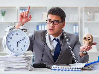 Businessman smoking holding human skull and an alarm clock in th