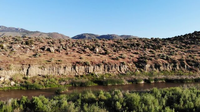 rone hover over green desert canyon and muddy creek with mountain background