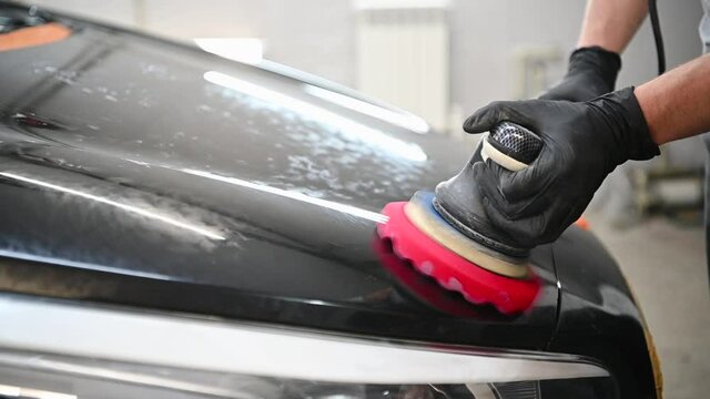 Male auto mechanic polishing a black car body with polishing machine for remove scratches