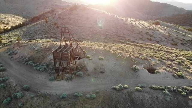 Drone orbit around mining head frame in nevada desert at sunset with sun flares.