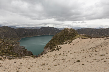 view of Quilotoa lake, Ecuador with a sandy hill and cloudy sky