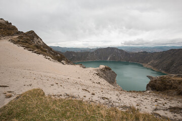 view of a volcanic lake in South America behind a hill of rock and sand