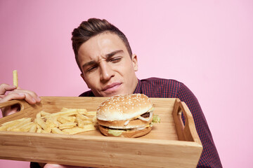 Man with fast food eating hamburger french fries pink background