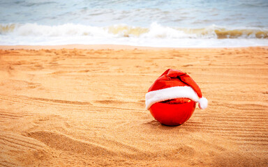 red christmas ornament in santa hat on sand beach