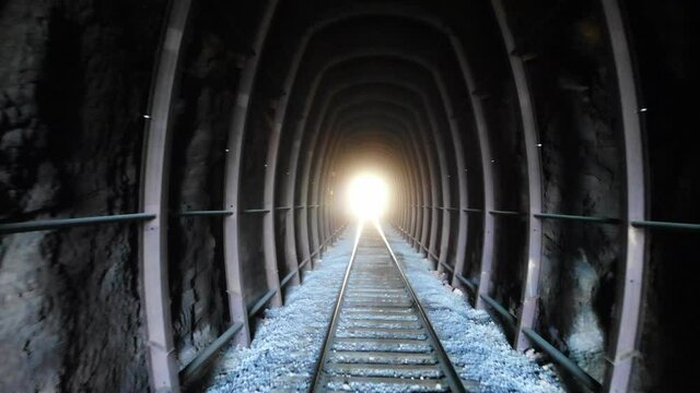 Drone flight down dark mining tunnel daylight shining at the end