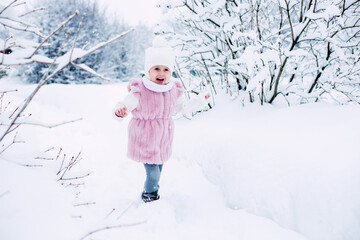 .A little girl in a pink fur coat stands in the middle of a snow-covered park