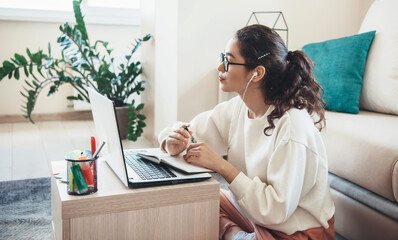 Attentive caucasian woman with glasses is having online lessons while using headphones and laptop