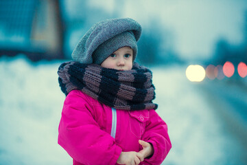 .A little girl stands in the snow by the road in the evening