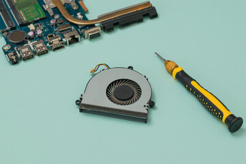 Cooling fan, screwdriver and laptop motherboard on a blue background.