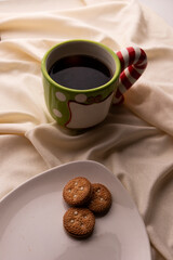 Cafe y Galletas para Santa Clause para navidad. Plato con galletas sobre la cama con piñas navideñas. Pocillo grande en verde y rojo