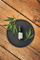 Cannabs medical product, CBD oil, with hemp leaves on a black dish on a wooden table. Flat lay. Mockup Copy spase