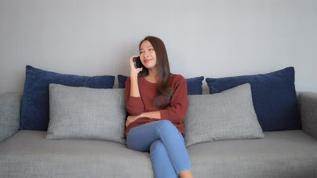 Attractive young woman talking on a mobile phone while sitting on a couch in her living room.