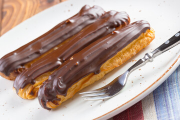 Chocolate eclairs on white plate on wooden table