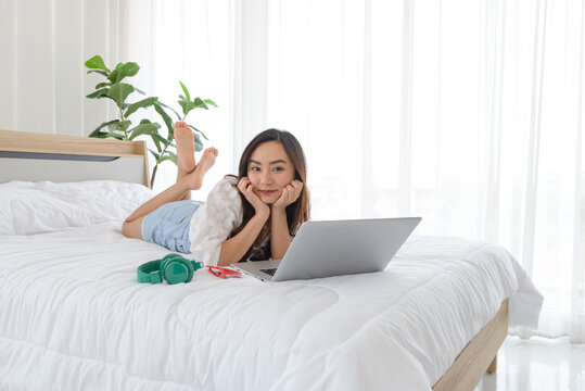 Beautiful young Asian woman relaxing and using a lapto on her bed.