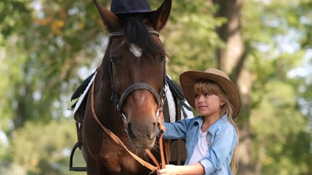 Cute little girl with long hair stroking a beautiful horse outdoors. Pet therapy