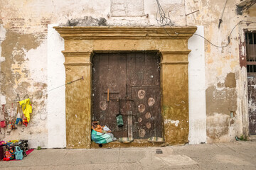 Fototapeta na wymiar Old church door with colorful selling goods of a street vendor, Cartagena, Colombia