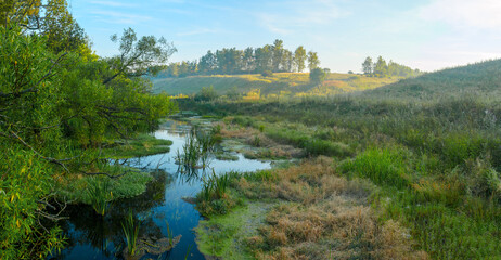Tranquil hazy landscape with small river at sunrise